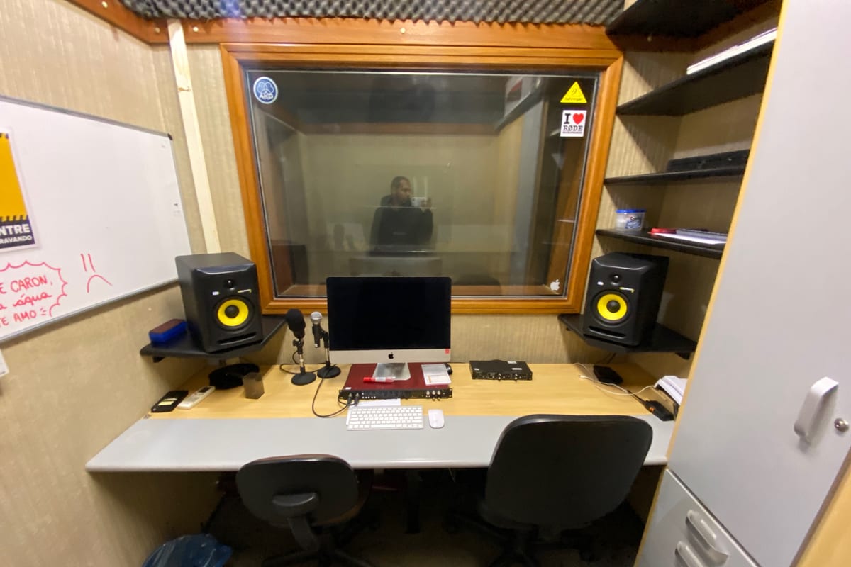 Voiceover booth — AKG large-diaphragm condenser on a boom, KRK Rokit monitors flanking the screen, acoustic treatment on the wall behind.