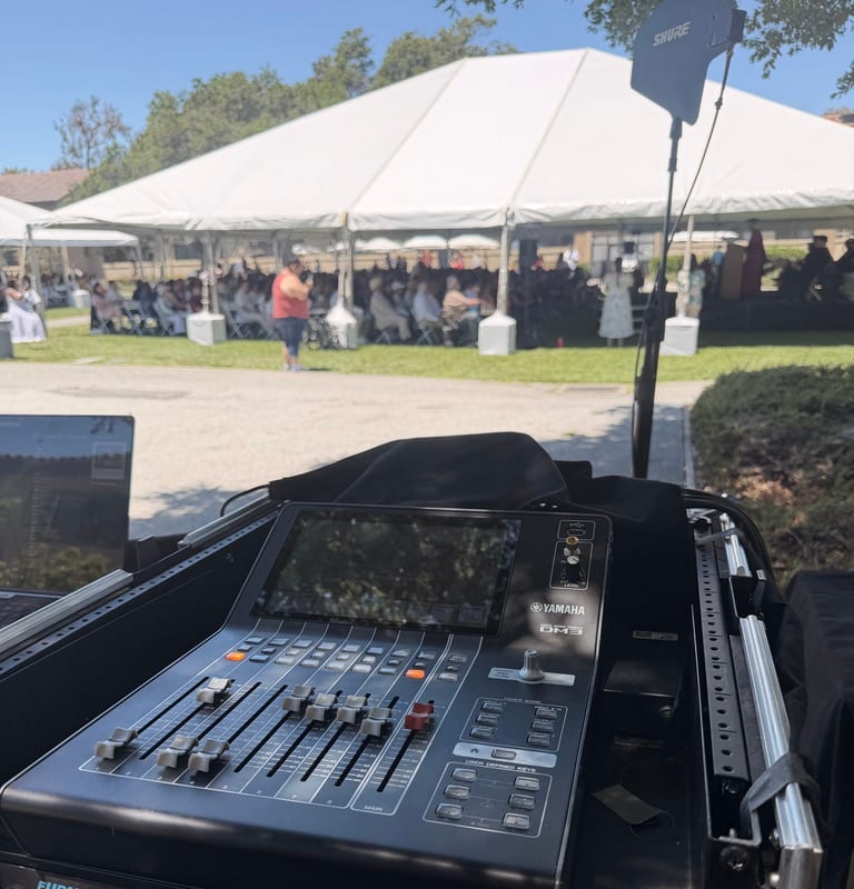 Yamaha QL5 console set up under a white event tent on grass — natural daylight FOH on an outdoor corporate stage.