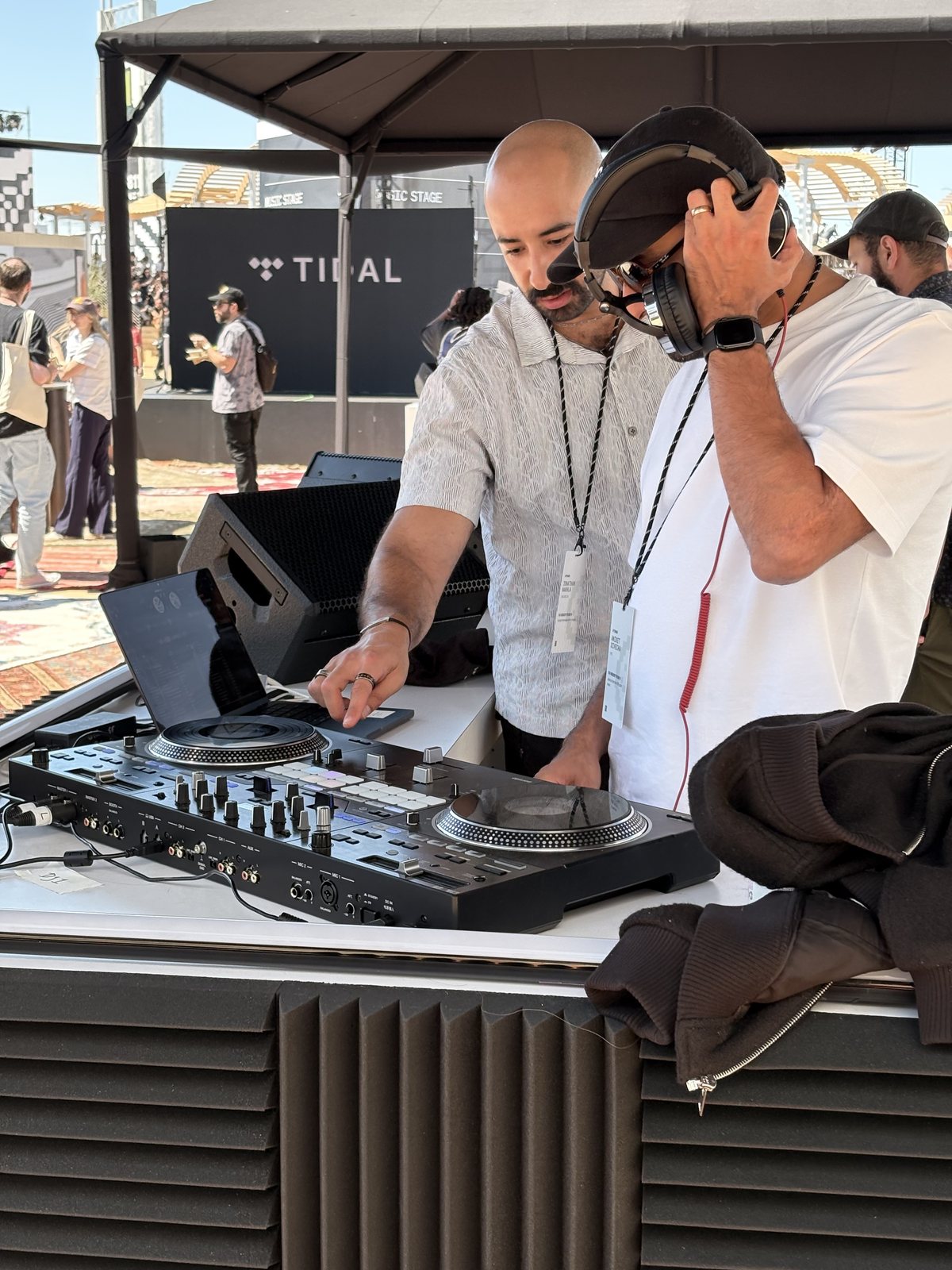 Victor in headphones at the Tidal-stage playback console — Pioneer-style decks at front-of-house, the TIDAL banner and event tents behind him.