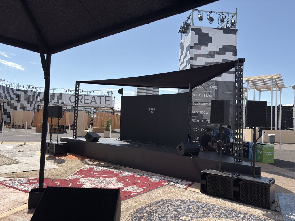The Tidal stage at the Block event — a line array and subwoofers flanking the deck, a multi-stage venue directory sign behind, rugs and shade tents on the ground.