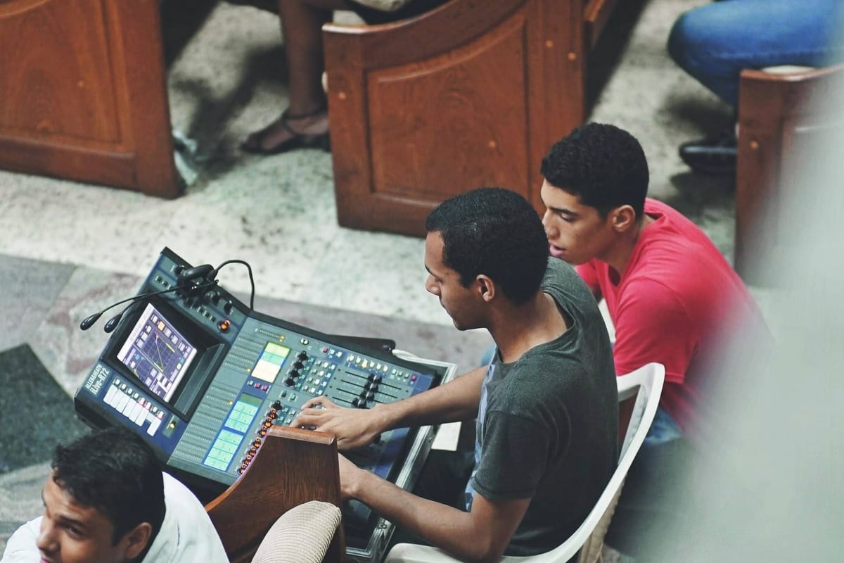 Bird's-eye angle of Victor at a Roland V-Mixer — both hands working the console at once, a second engineer leaning in.